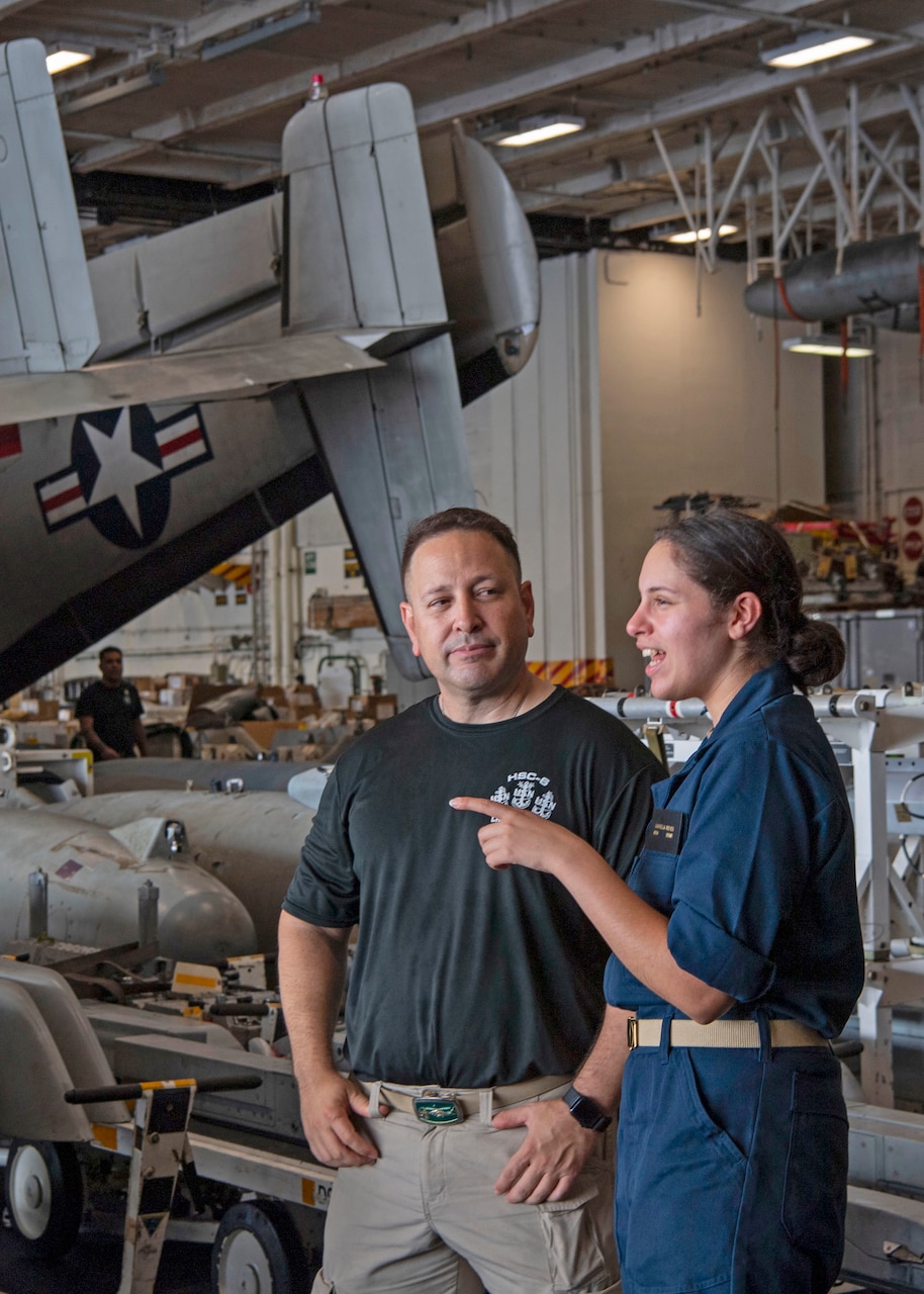 Senior Chief Aviation Machinist's Mate Dan Reyes and his daughter, U.S. Midshipmen 2nd Class Gabriella Reyes, from Miami, Florida talk in the Hanger Bay of the aircraft carrier USS Nimitz (CVN 68) in the South China Sea, June 11, 2025. Nimitz is underway in the U.S. 7th Fleet area of operations on a scheduled deployment, demonstrating the U.S. Navy's unwavering commitment to a free and open Indo-Pacific.