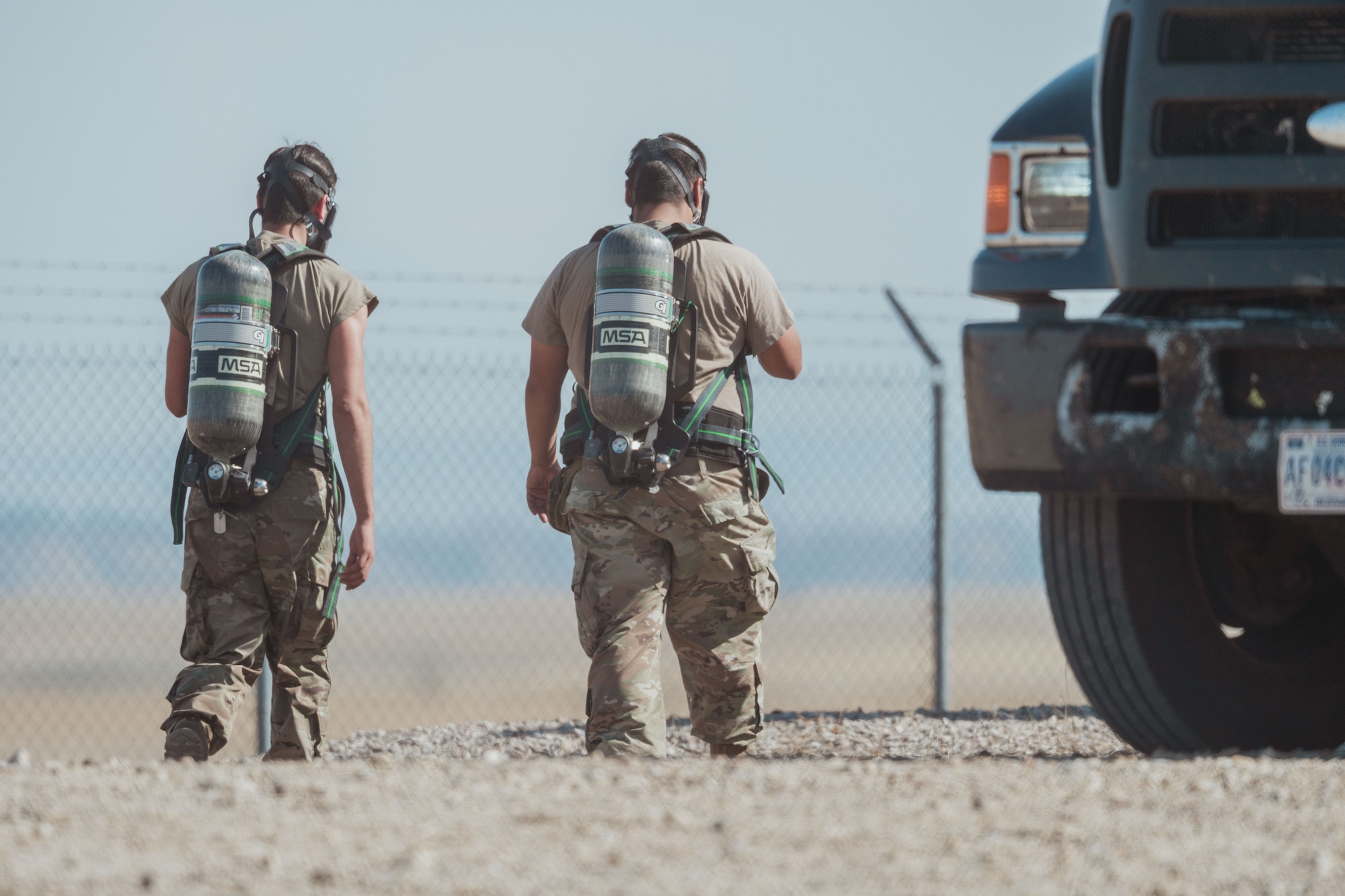 Two Airmen walking away with oxygen tanks on their backs.