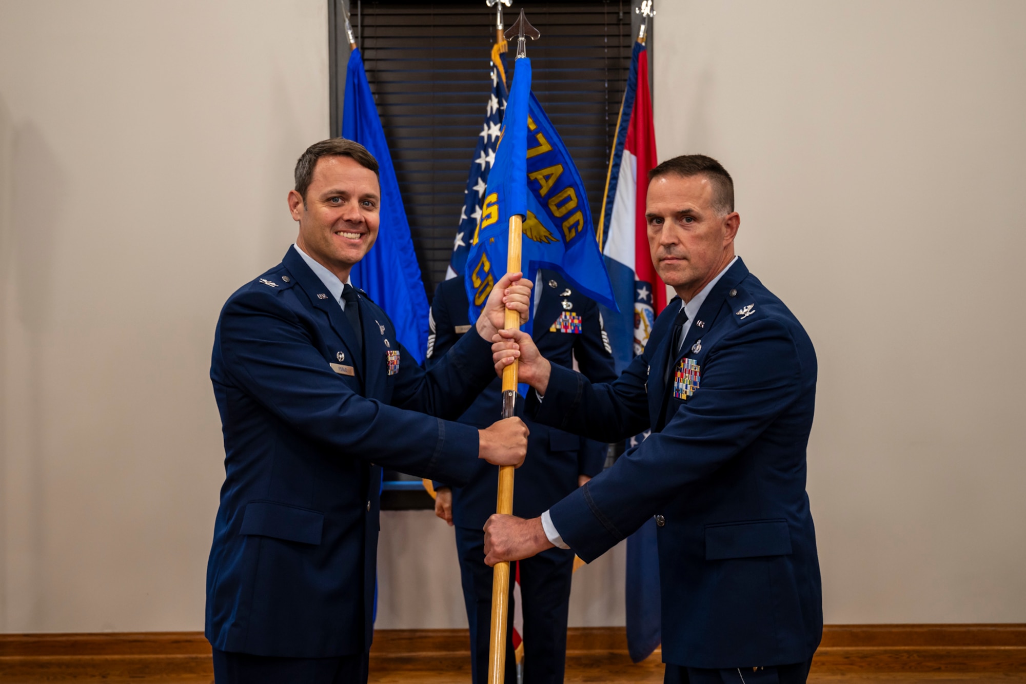 Two Airmen in uniform, identified as 157th AOG commander Col. Joshua Fogle and 257th COS commander Col. Glen Hawley, pose with the guidon of the newly designated 257th Combat Operations Squadron.