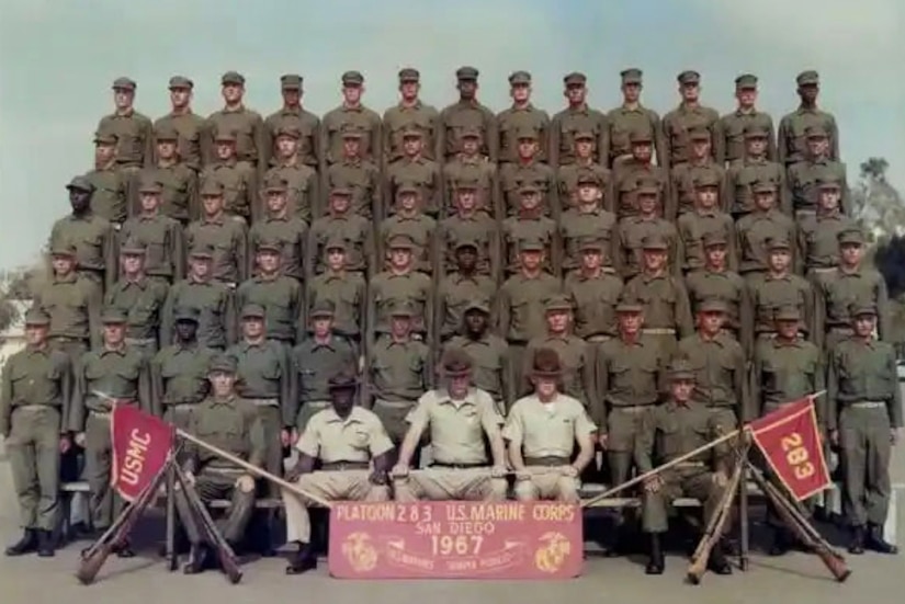 A platoon of Marines wearing military uniforms sitting and standing on bleachers.