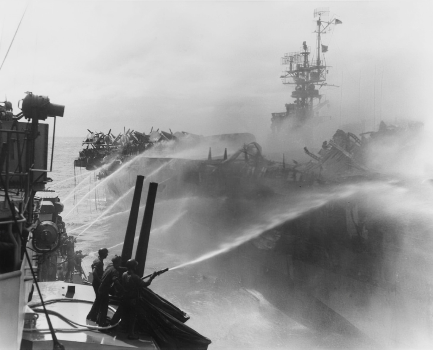 The light cruiser USS Reno (CL 96) moves in close to the burning Princeton so its crews can hose down the badly damaged carrier.
