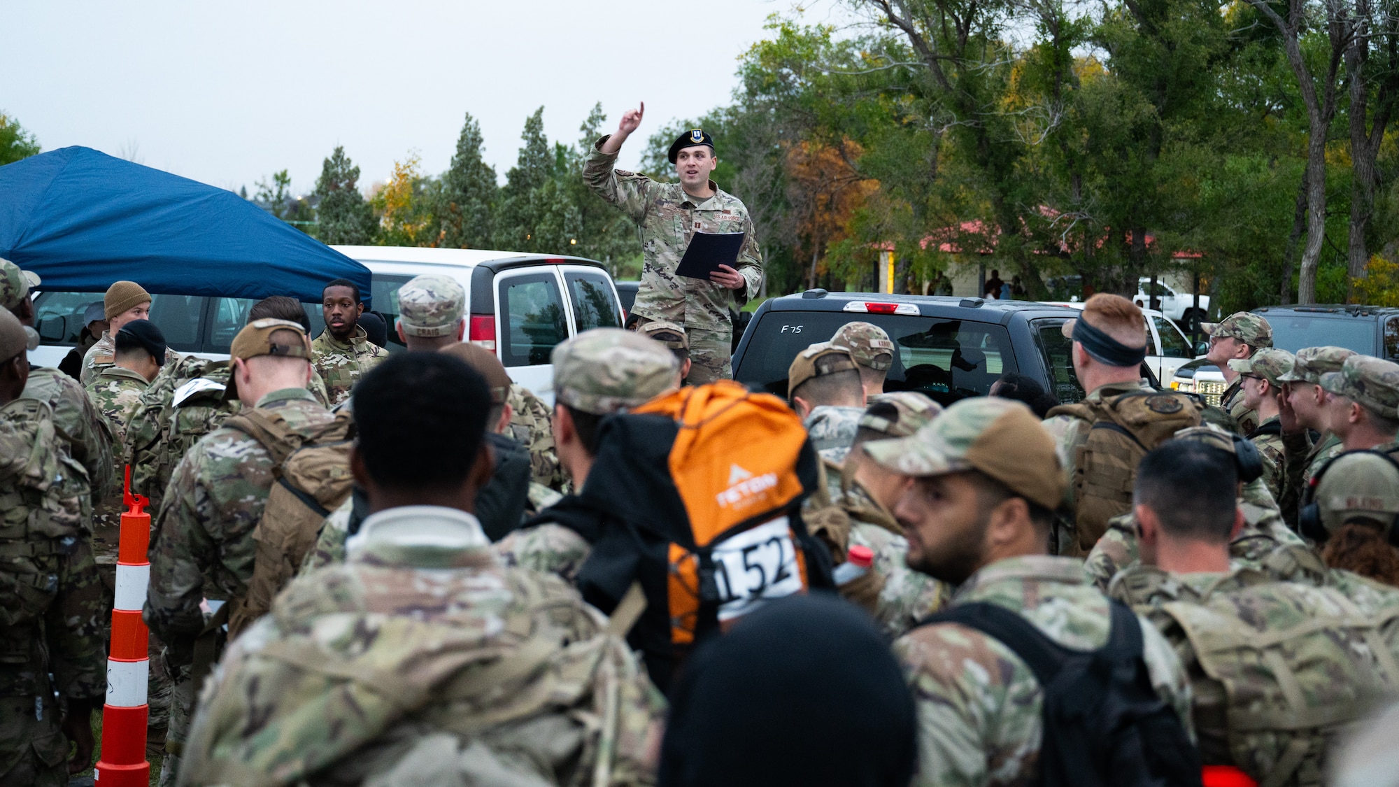 Several Airmen listen to a safety brief from an officer, who stands on the back of a truck.