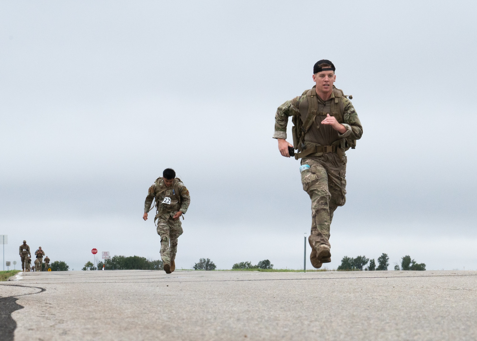 Airmen wearing rucksacks sprint toward a finish line.