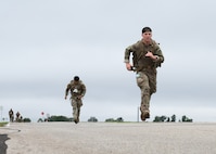Airmen wearing rucksacks sprint toward a finish line.
