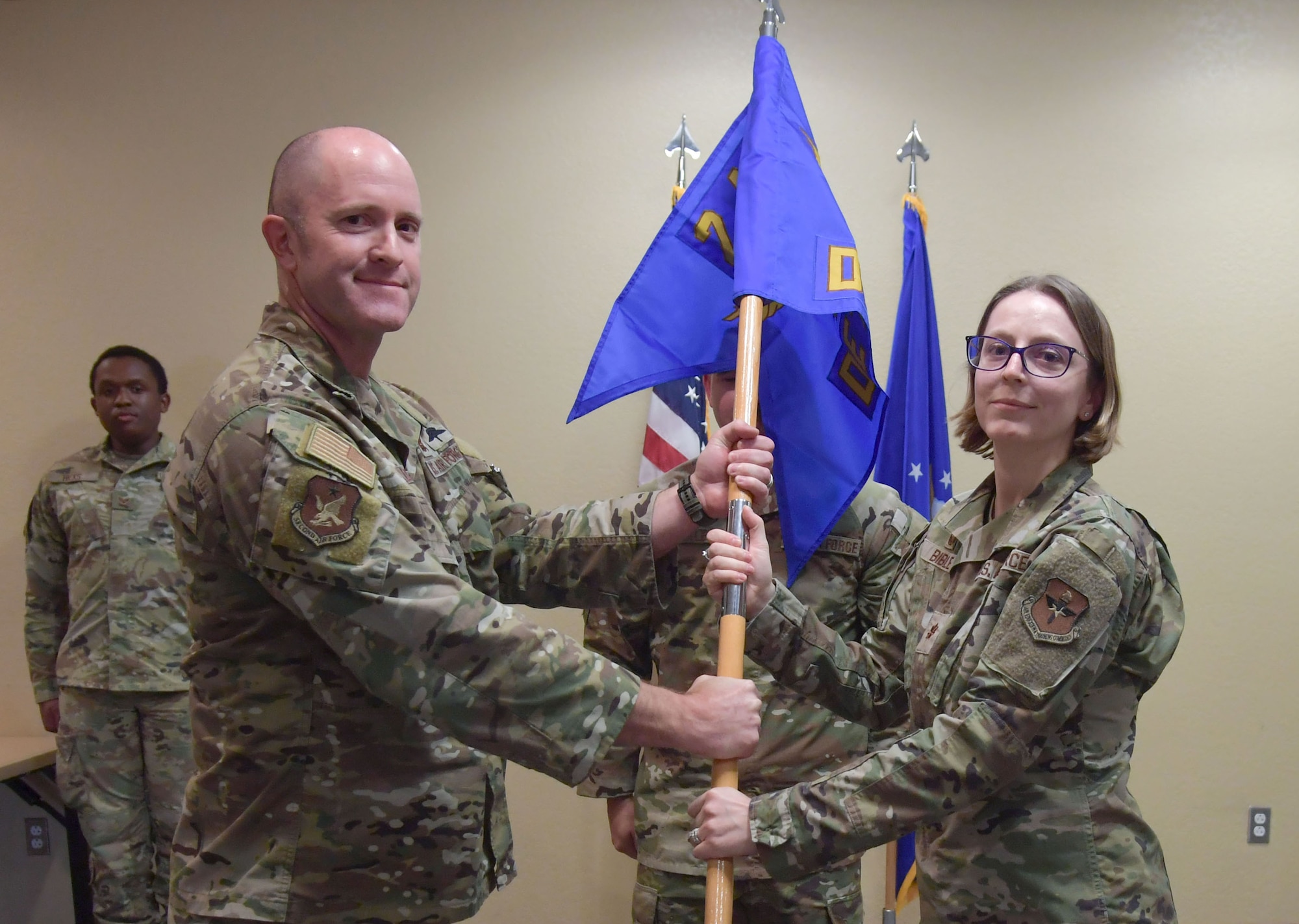 A man and woman in military uniform hold the handle of a unit flag