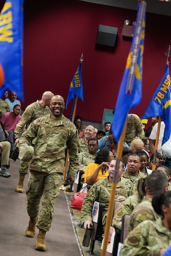 A smiling Air Force colonel walks down an aisle between airmen.