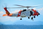 A rescue swimmer from U.S. Coast Guard Air Station Astoria dangles below an MH-60 Jayhawk helicopter as it hovers above Elliott Bay near Seattle, Washington, Aug. 1, 2023. The demonstration was part of the Parade of Ships for the annual Seafair festival. (U.S. Coast Guard photo by Petty Officer 2nd Class Steve Strohmaier)