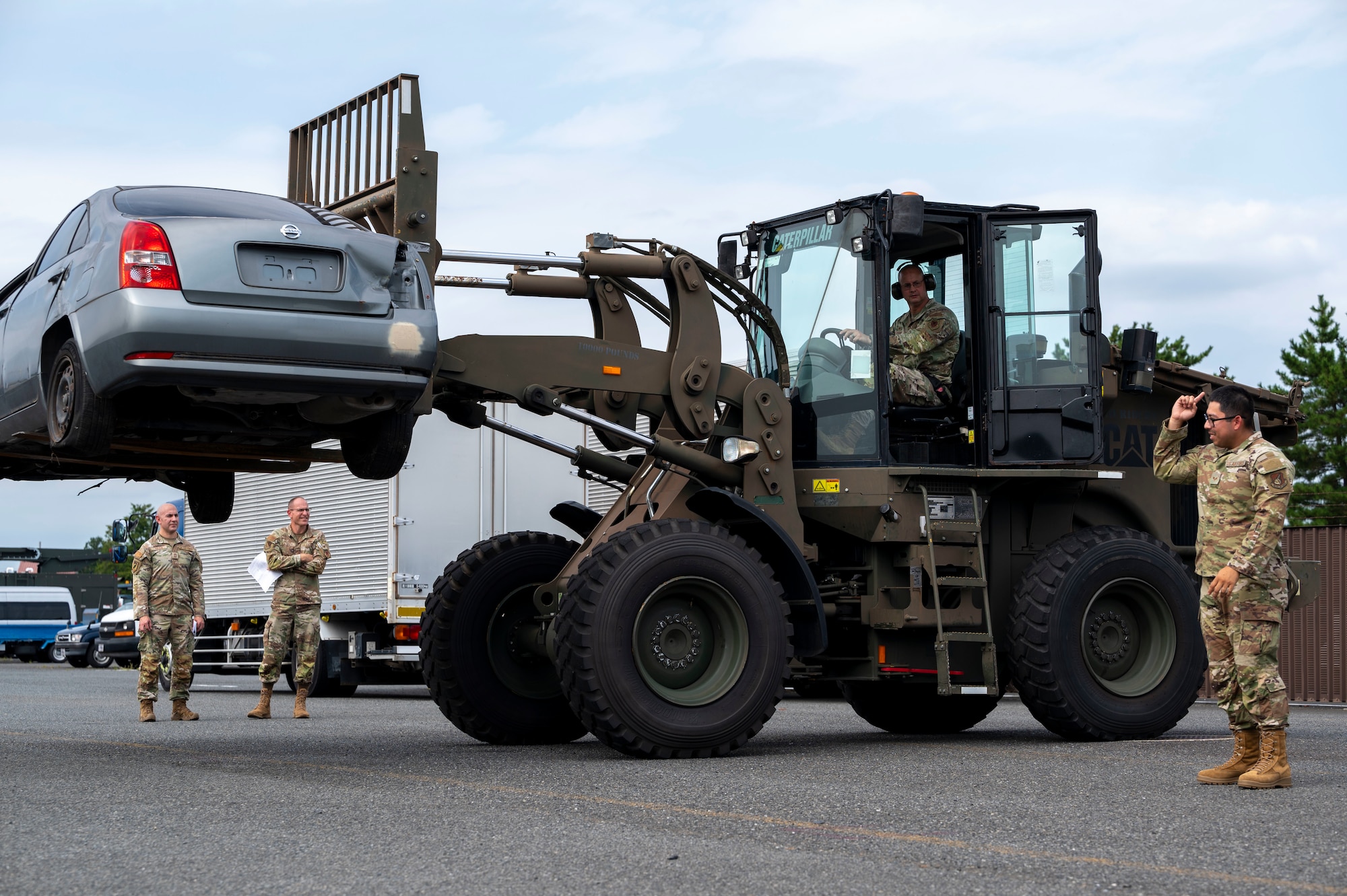 A military member uses a forklift to flip a car over.