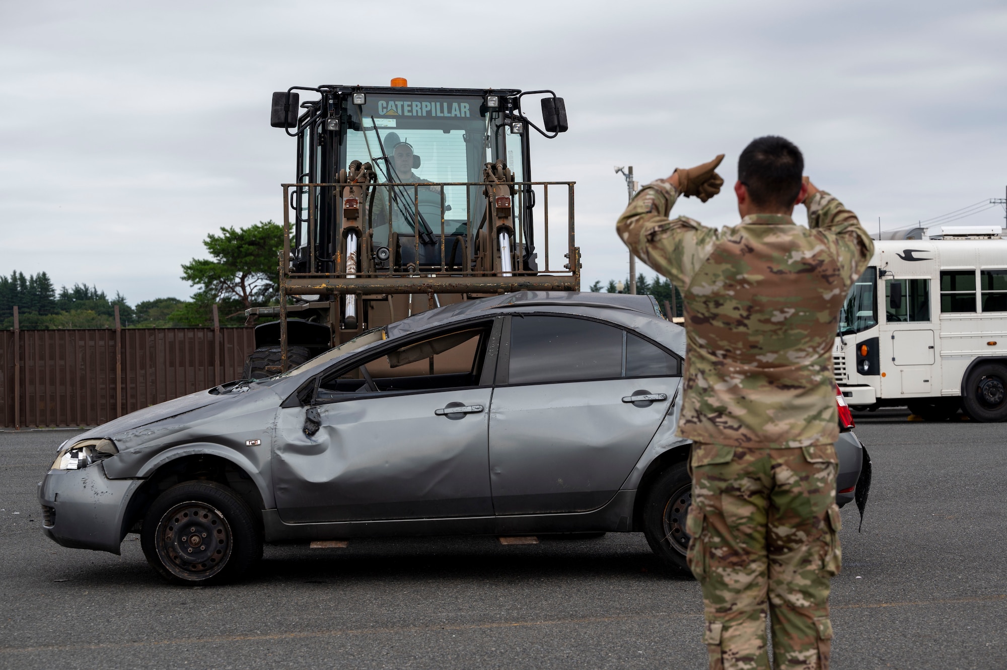 A military member signals to another military member using a forklift.