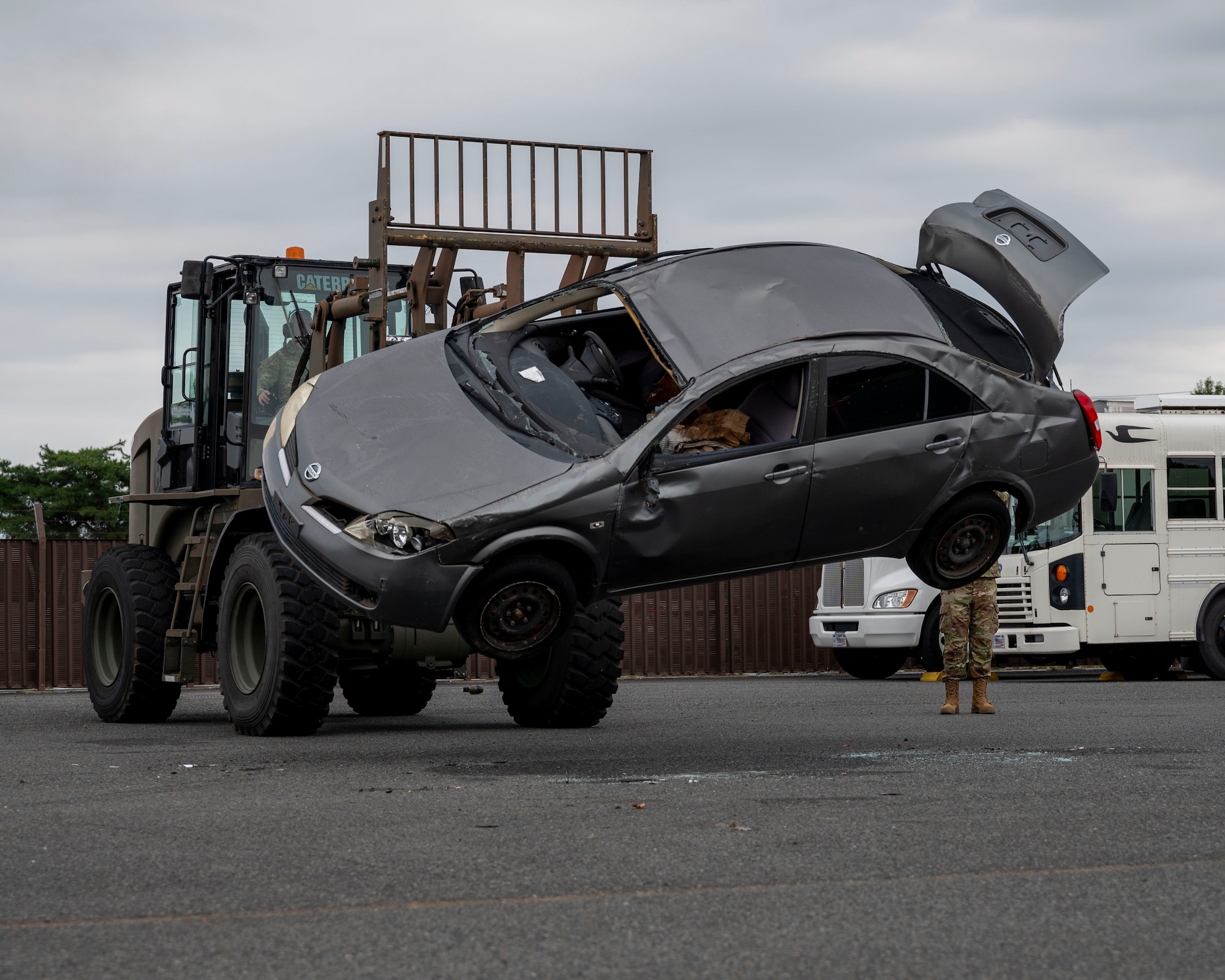 A military member uses a forklift to flip over a car.