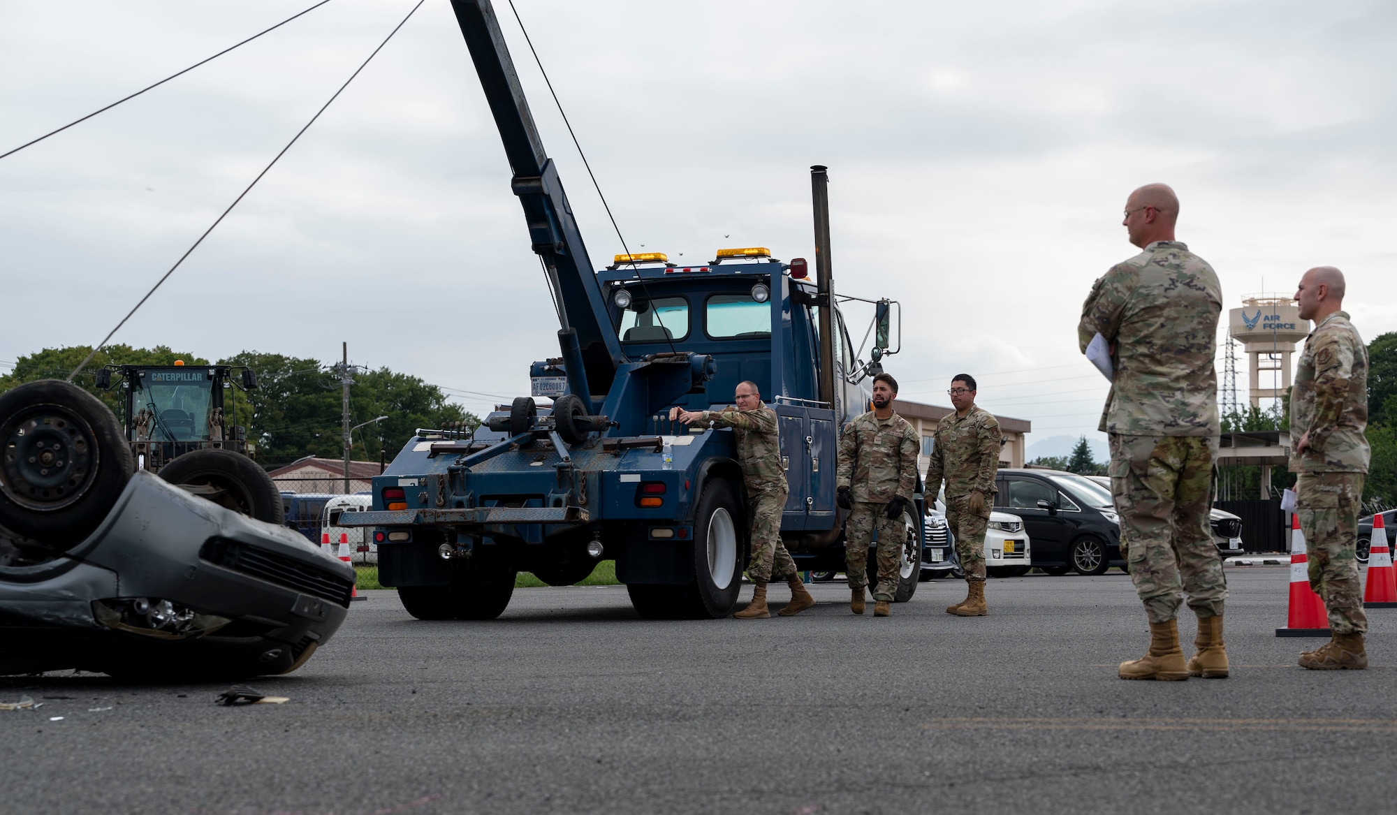 A military member uses heavy equipment to turn a car over.