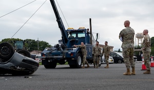 A military member uses heavy equipment to turn a car over.