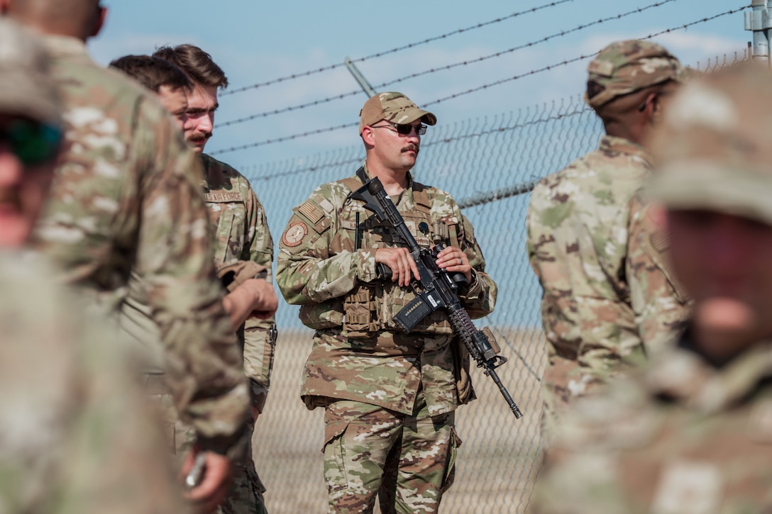 An Airman with a gun stands by with other Airmen around him.