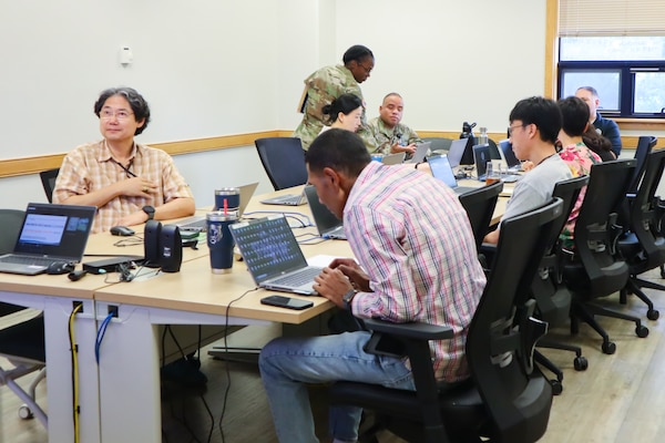 A group of seven people sit around a conference room table working on computers.