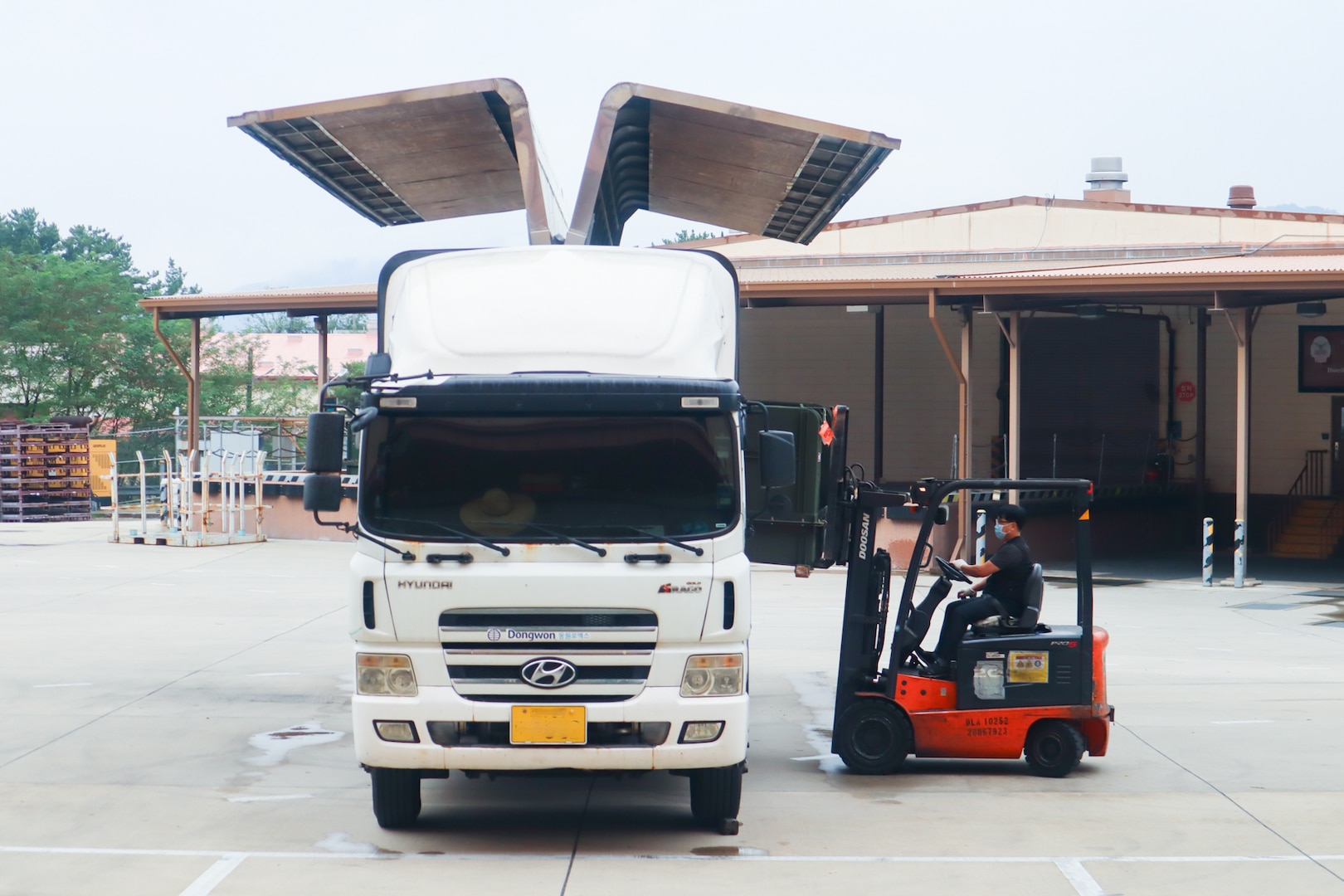A person in a forklift loads a pallet into a transportation truck outside of a warehouse.