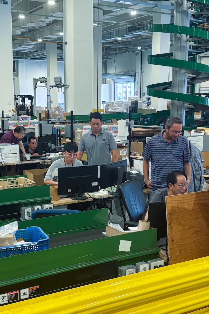 A group of people work at multiple computers inside of a large warehouse.