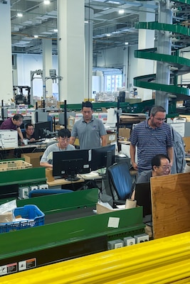 A group of people work at multiple computers inside of a large warehouse.