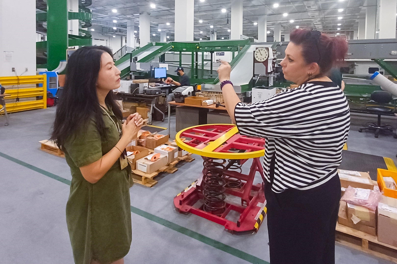 Two women speak to each other in a large warehouse.