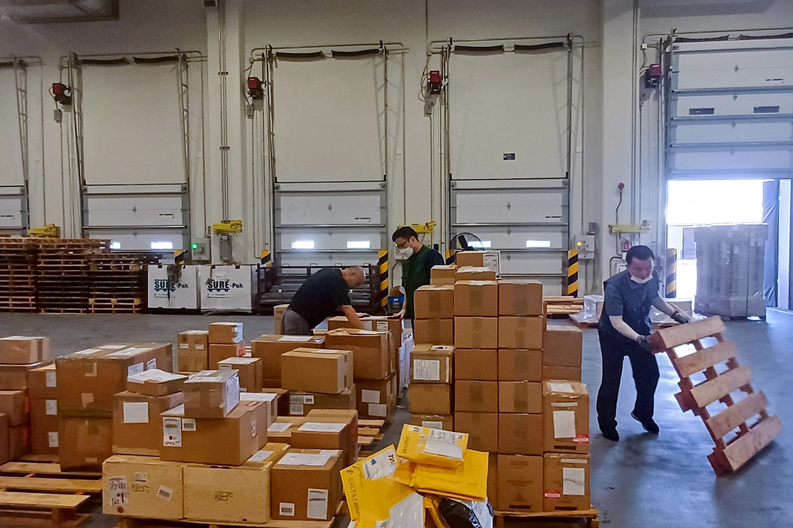 People move boxes and pallets in a large warehouse.