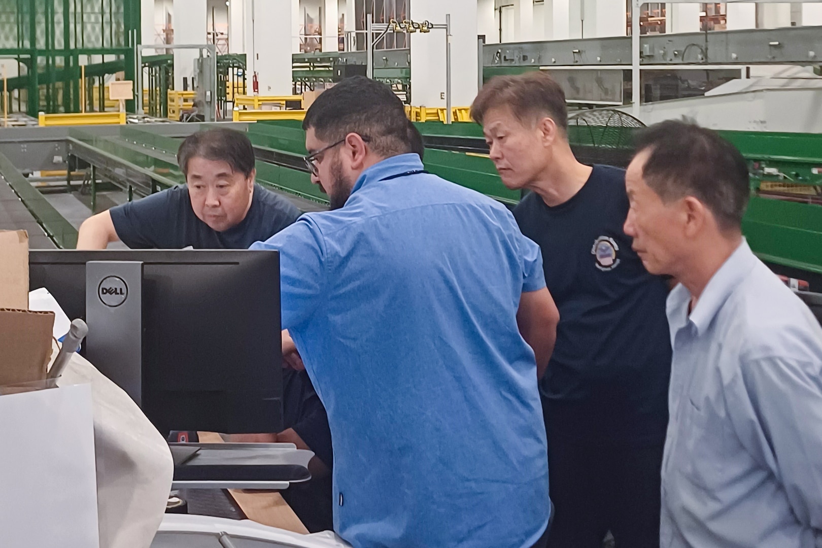 A group of people stand around a computer screen in a large warehouse.