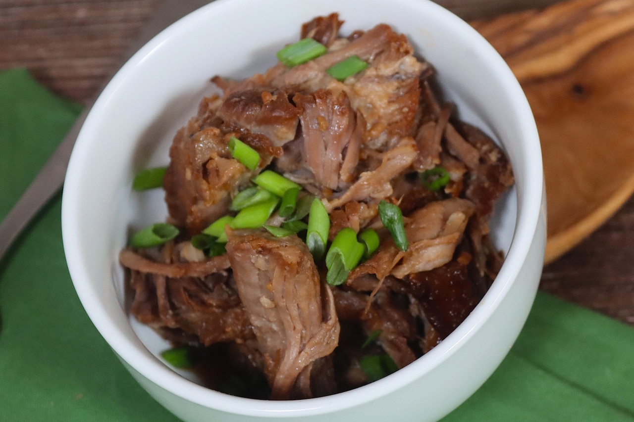 A bowl contains strips of beef and chopped shallots.