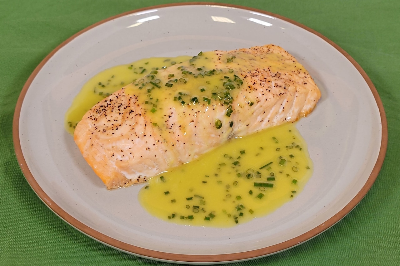 A piece of salmon covered in a sauce sits on a plate.