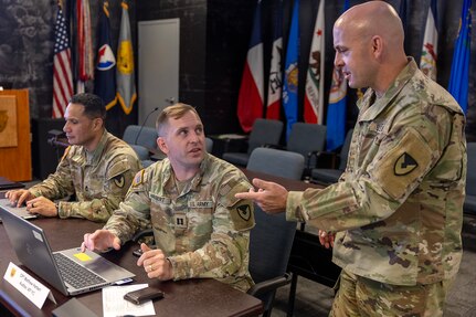 Capt. Matthew Harbert, 45th Finance Center auditor, talks with Master Sgt. Jerrod Newman, 45th FC Team A noncommissioned officer in charge from Fort Knox, Kentucky, as Master Sgt. Sitanimoa Filimoeulie, 45th finance operations manager, works at his computer during a staff exercise in the Mark Sullivan Auditorium at the Maj. Gen. Emmett J. Bean Federal Center in Indianapolis Sept. 18, 2025. The four-day exercise brought together elements from the 45th FC’s headquarters and three geographically separated teams to assess the unit’s operational capacity and limitations while enhancing its future operational reach for large scale and multidomain operations. (U.S. Army photo by Mark R. W. Orders-Woempner)