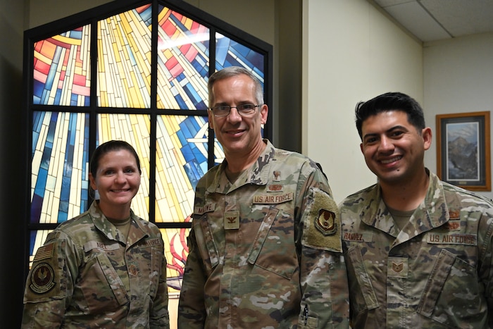 Chief Master Sgt. Jennifer Abel, Senior Enlisted Leader for Religious Affairs, Chaplain (Col.) Dale Marlowe, Air Force Materiel Command Chaplain, and Tech. Sgt. Tyler Ramirez, Readiness and Resource Support Manager, pose for a photo in the chaplain’s office at AFMC headquarters. They are wearing OCP's and standing in front of a stained-glass window.