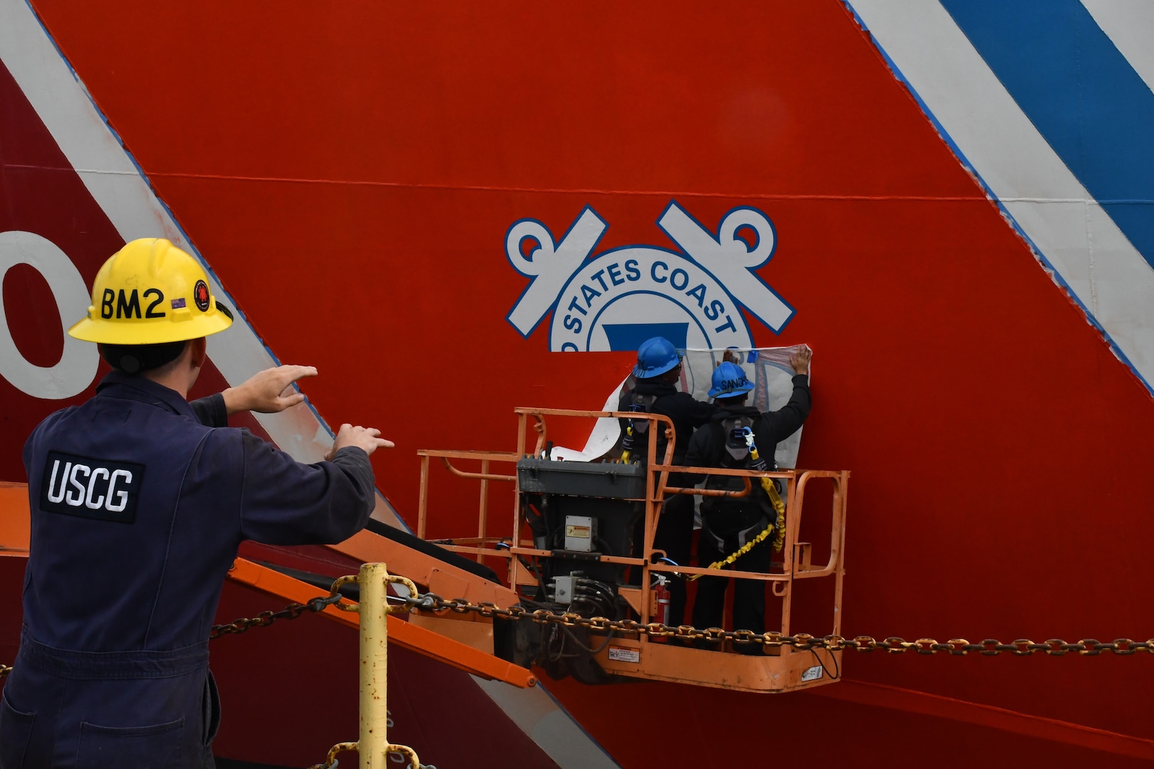 A boatswain’s mate assists the crewmembers of the USCGC Polar Star (WAGB 10) in helping paint the racing stripe on the hull of the cutter in Vallejo, Calif., Aug. 1, 2025. Additional major work completed includes removing the centerline shaft for servicing and inspection, exchanging all three propellers, and renewing both forward and aft main deck surfaces. (U.S. Coast Guard photo by Seaman Reagan Vasbinder)