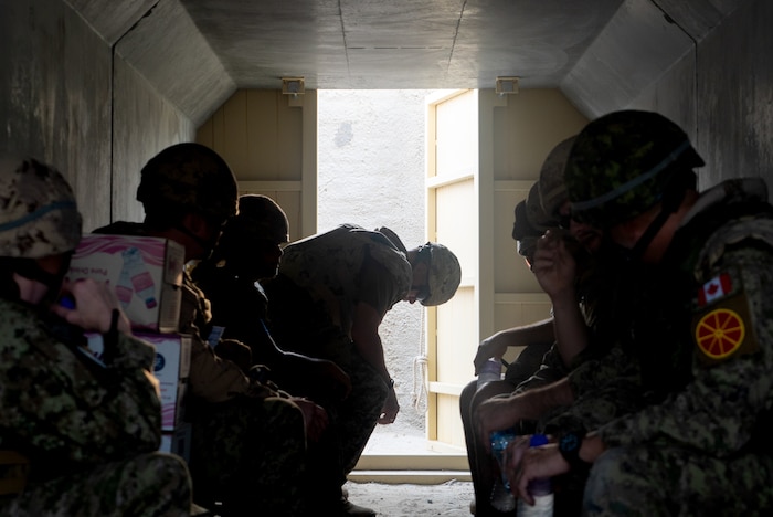 A collection of silhouettes line either side of the frame inside a bunker with an open bunker door in the middle