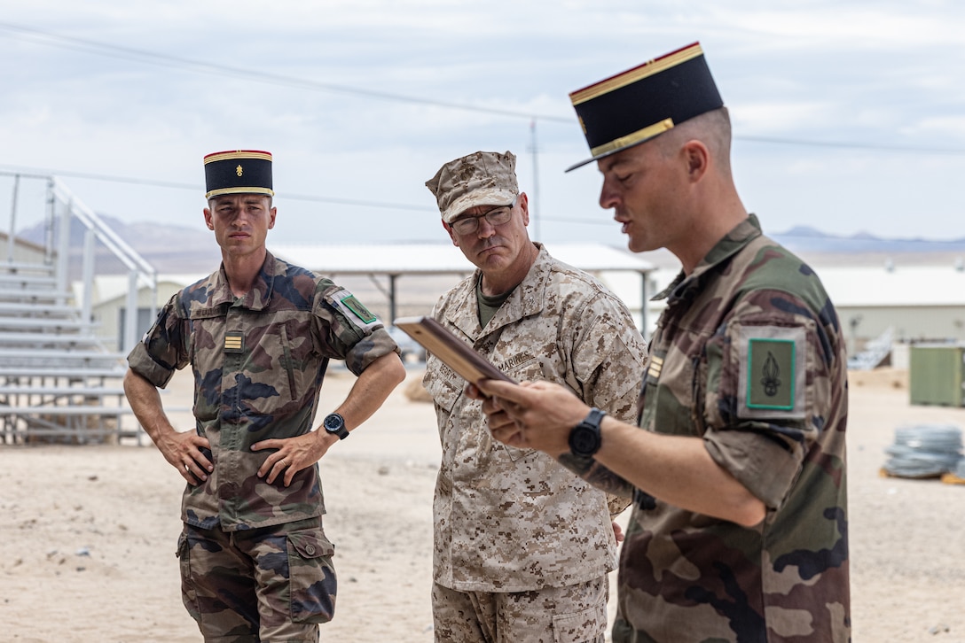 A French Foreign Legionnaire with 2nd Foreign Infantry Regiment, 6th Light Armored Brigade, reads a plaque during an award ceremony as part of Service Level Training Exercise 4-25, on Marine Corps Air-Ground Combat Center, Twentynine Palms, California, Aug. 23, 2025. SLTE 4-25 is designed to be a challenging, realistic training environment that produces combat-ready forces capable of operating as an integrated Marine Air Ground Task Force across all domains of military operations. (U.S. Marine Corps photo by Lance Cpl. Judith Ann Lazaro)