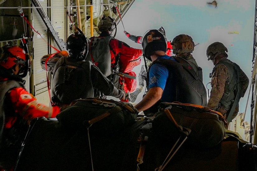 Four people stand at the door of an open aircraft and prepare to jump.