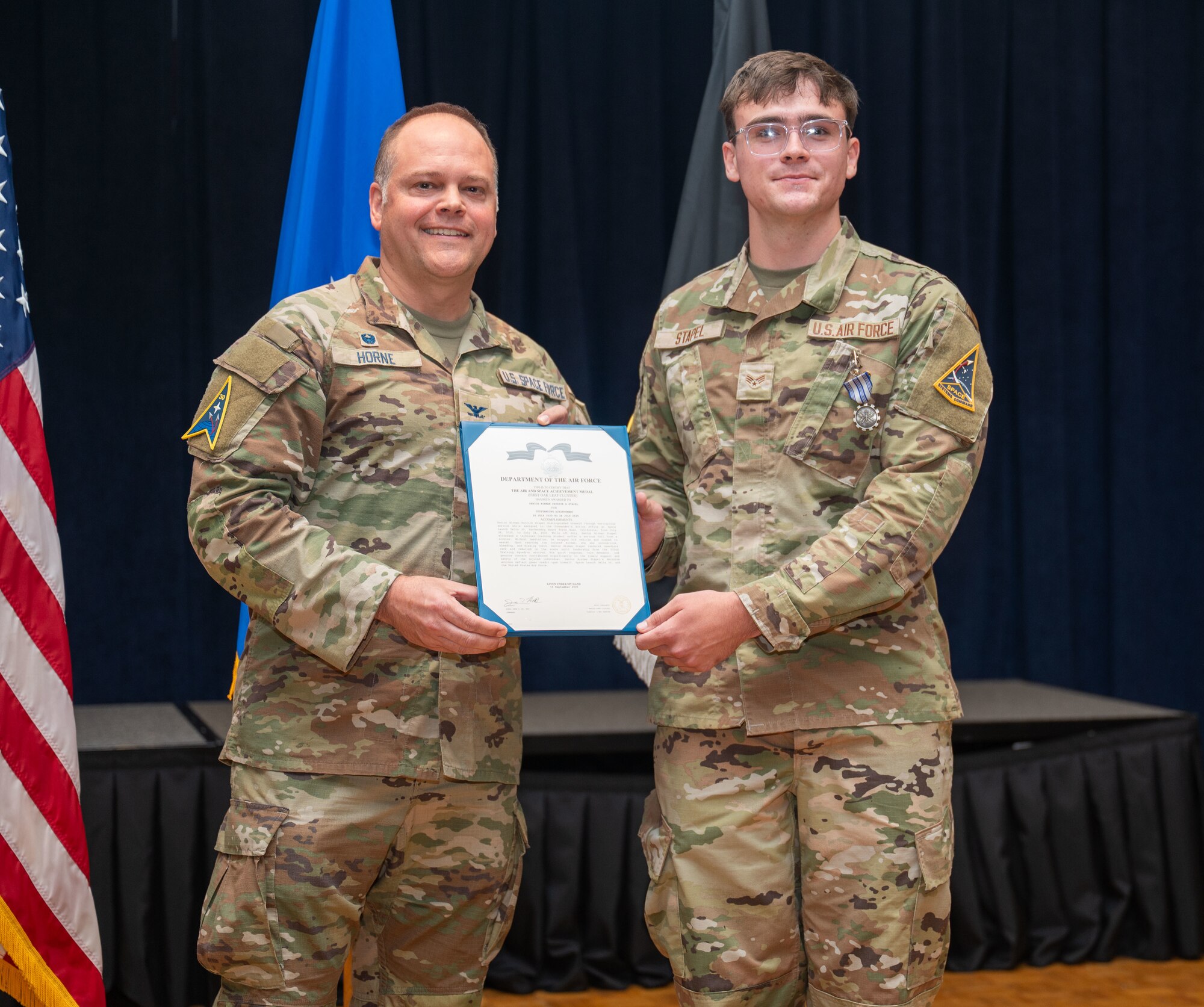 Two people stand on a stage and smile for a photo.