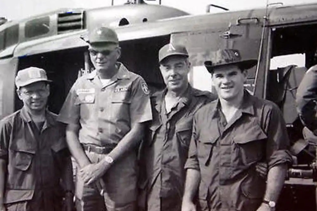 Four men in Army uniforms stand beside a helicopter.