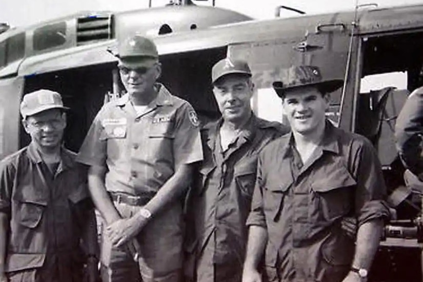 Four men in Army uniforms stand beside a helicopter.
