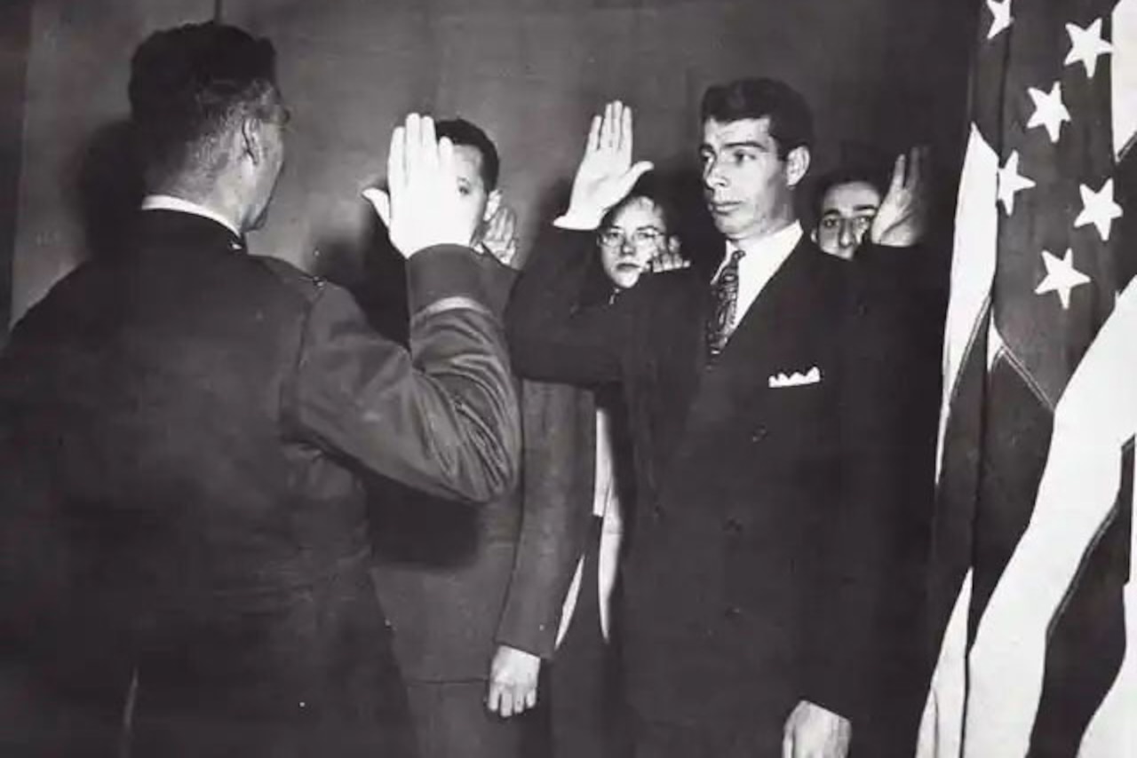 Men in suits beside an American flag raise their right hands.