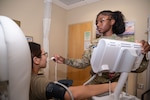 Uniformed service member uses thermometer on patient sitting in chair.