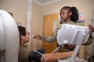 Uniformed service member uses thermometer on patient sitting in chair.