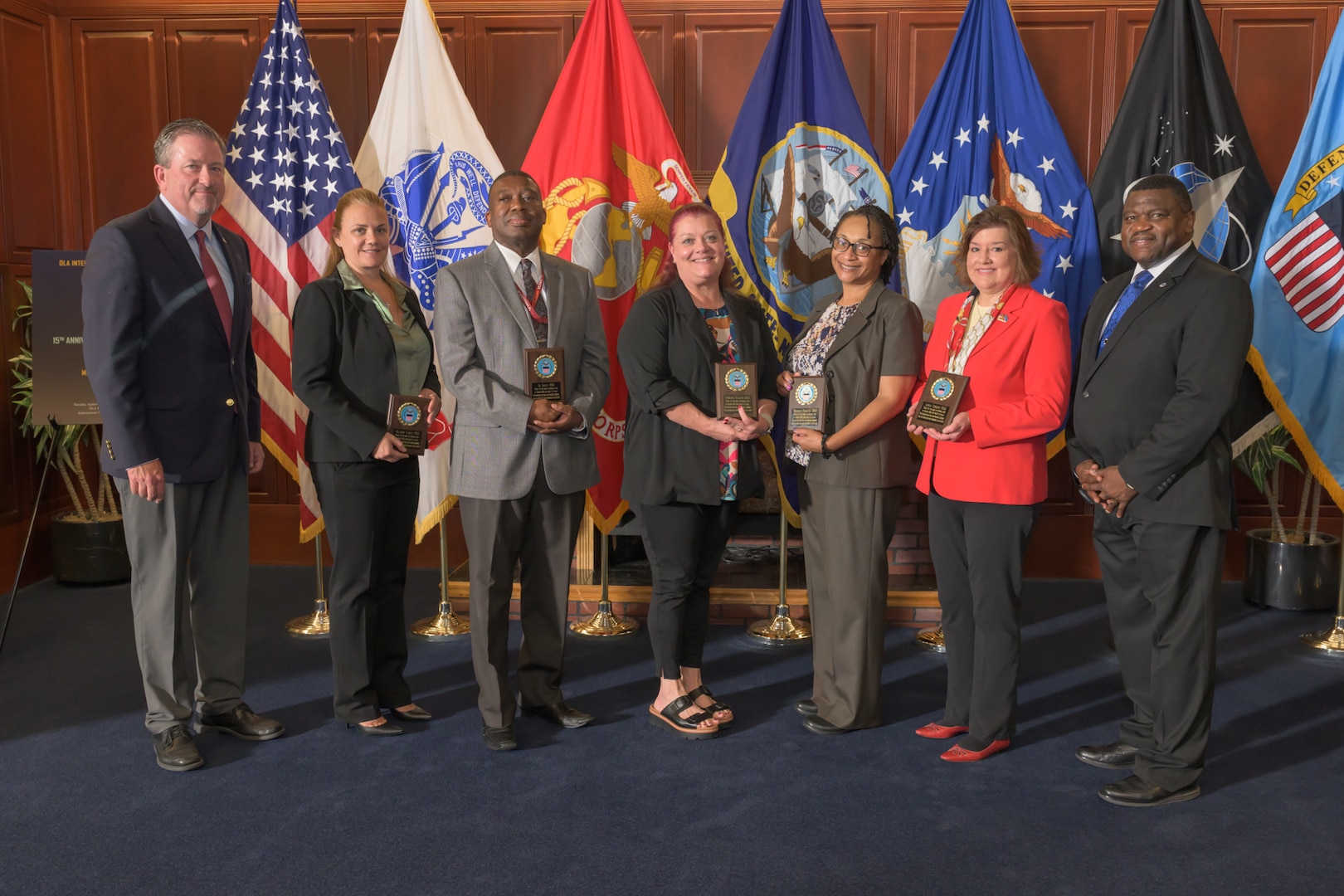 A group of people holding plaques stand in front of flags.