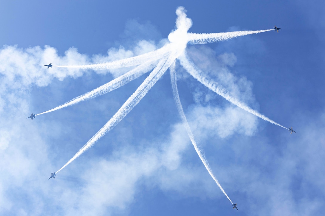 Six aircraft fly in different directions leaving behind white streaks in a blue sky.