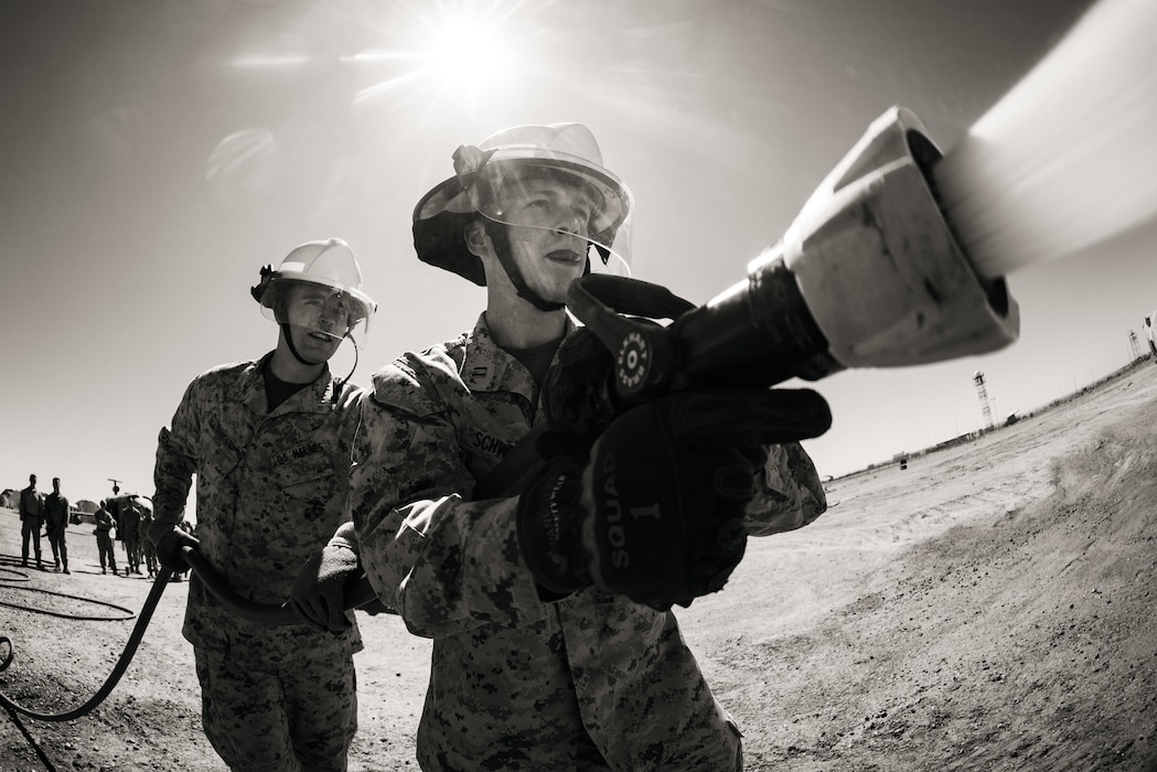 U.S. Marine Corps 1st Lt. Daniel Goddard, left, a California native, logistics officer with Marine Wing Support Squadron (MWSS) 174, Marine Aircraft Group 24, 1st Marine Aircraft Wing, and Capt. Austin Schweyen, a Washington native, logistics officer with MWSS 171, MAG 12, 1st MAW, extinguish a notional fire during an aircraft rescue and firefighting demonstration as part of Weapons and Tactics Instructor course (WTI) 1-26 at Marine Corps Air Station Yuma, Arizona, Sept. 15, 2025. WTI is a seven-week training event hosted by Marine Aviation Weapons and Tactics Squadron One (MAWTS-1) which emphasizes operational integration of the six functions of Marine aviation in support of the Marine Air Ground Task Force, Joint and Coalition Forces. (U.S. Marine Corps photo illustration by Lance Cpl. Micah Thompson)