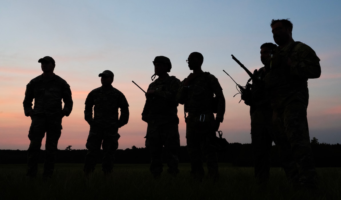 Six airmen with body armor and communication gear stand against a sunset background.