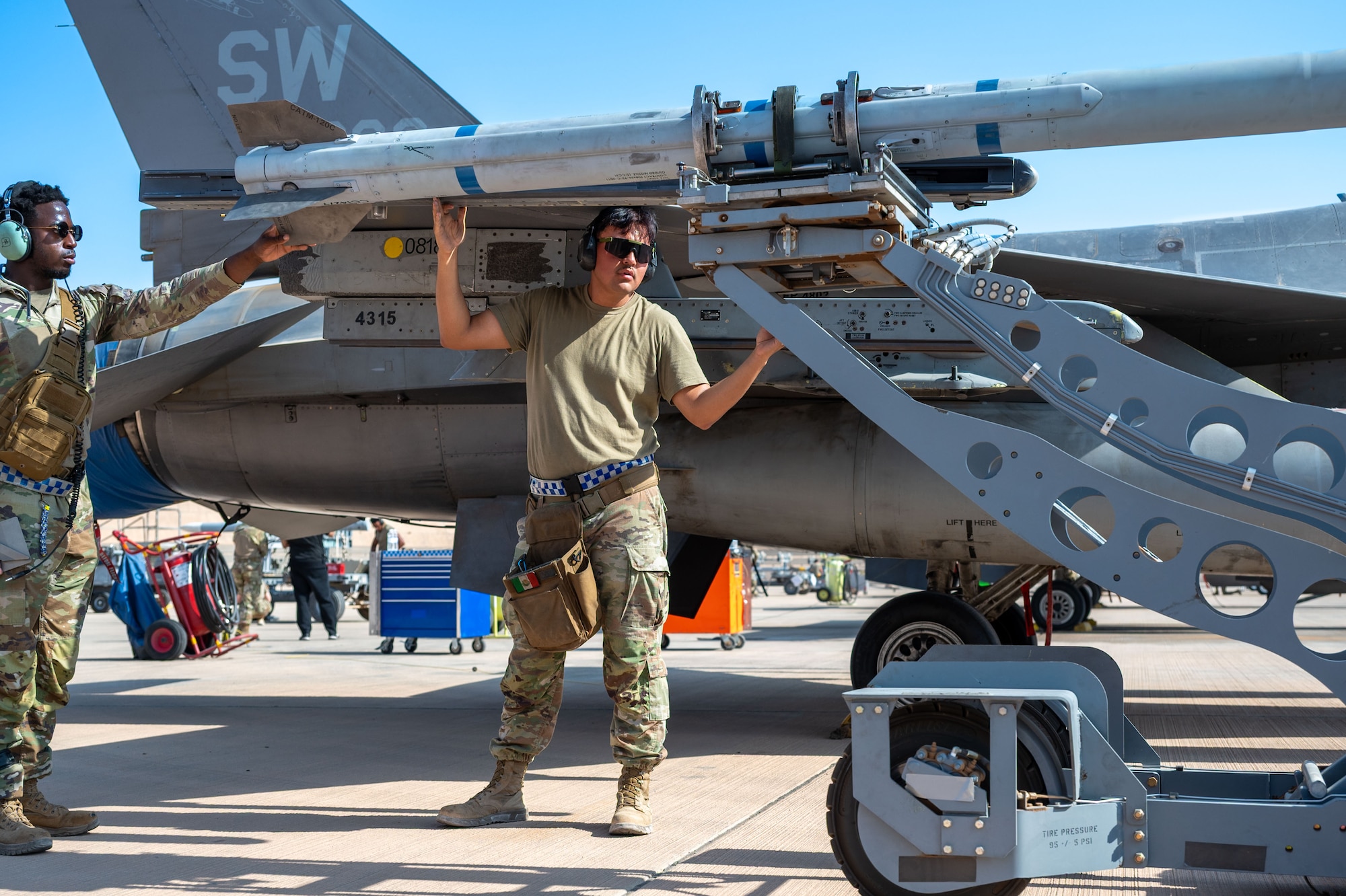 U.S. Air Force Airman 1st Class Adrion Hurd, 55th Expeditionary Fighter Generation Squadron weapons load crew member, and Staff Sgt. Oscar Fernández, 55th EFGS weapons load crew chief, guide an AIM-120 into place during a load competition.
