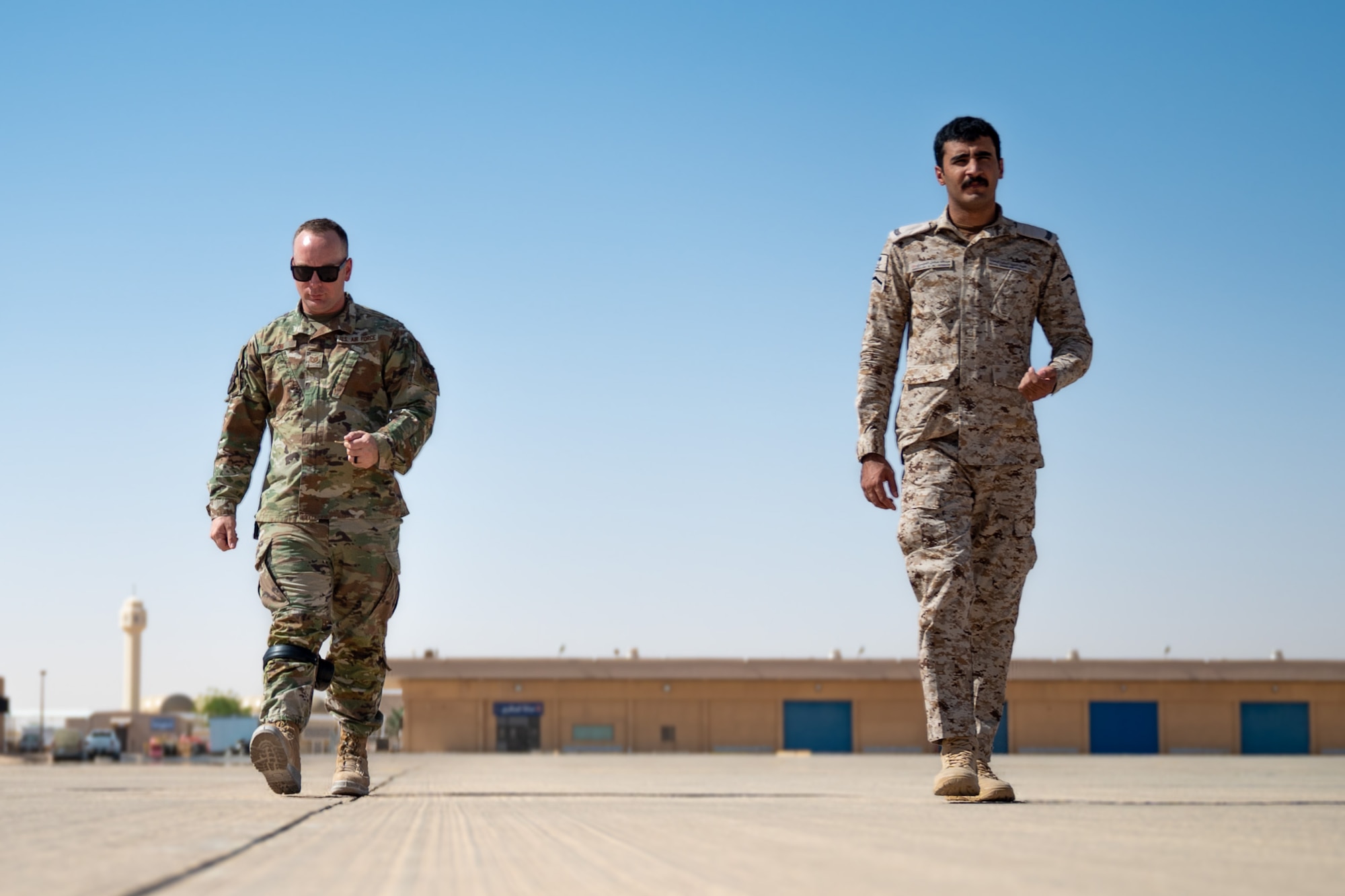 A USAF and RSAF service member walk down a flightline