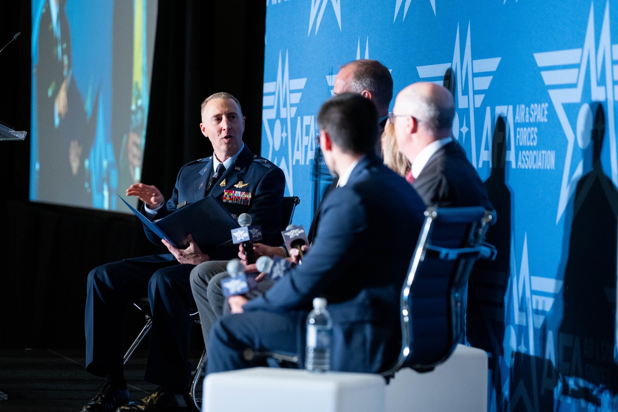 STARCOM leadership in uniform on stage with other panel guests. Speakers and listeners are sitting in chairs.