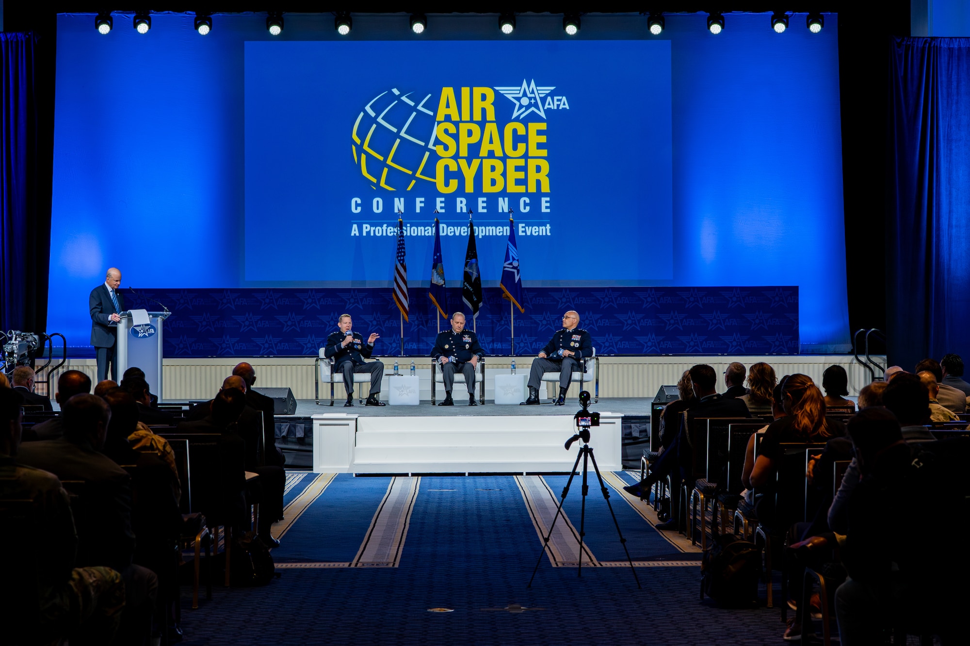 STARCOM leadership in uniform on stage with other panel guests. Speakers and listeners are sitting in chairs.