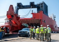 A group of people wearing hard hats and reflective vests stand next to a cargo ship