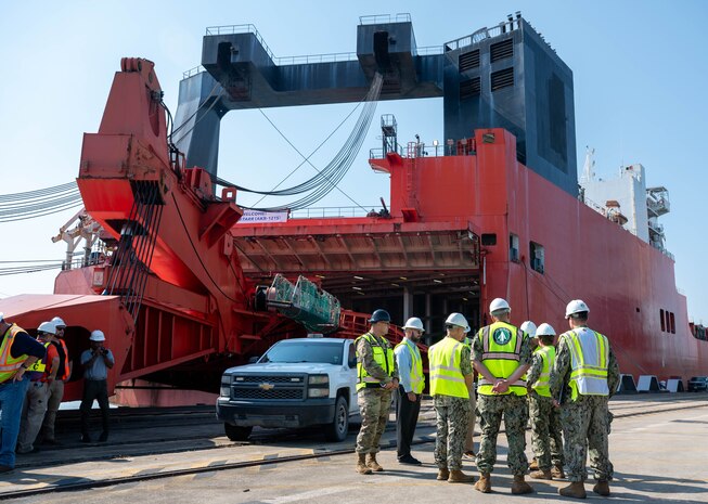 A group of people wearing hard hats and reflective vests stand next to a cargo ship