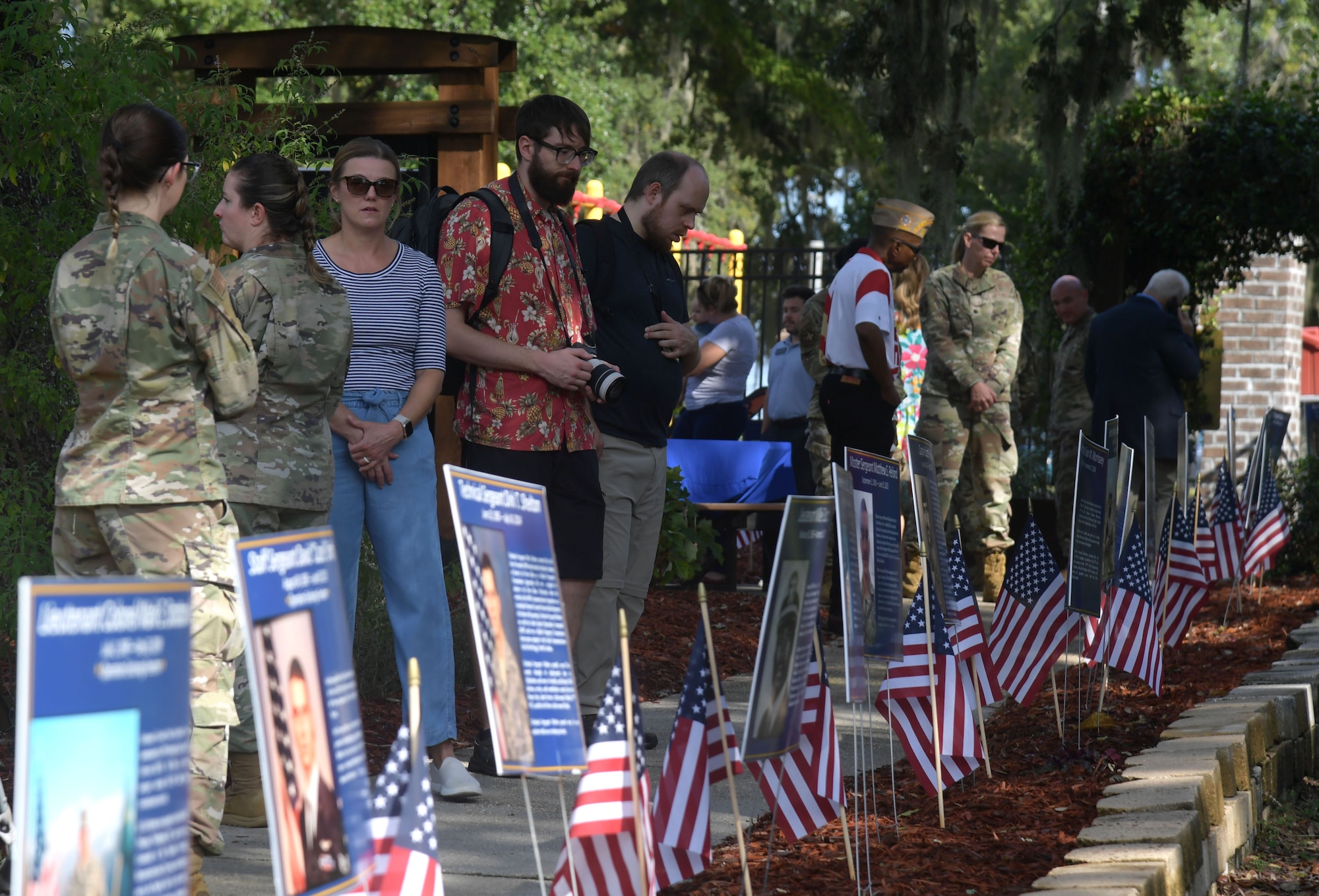 A group of people gather around a row of memorial posters of fallen heroes.