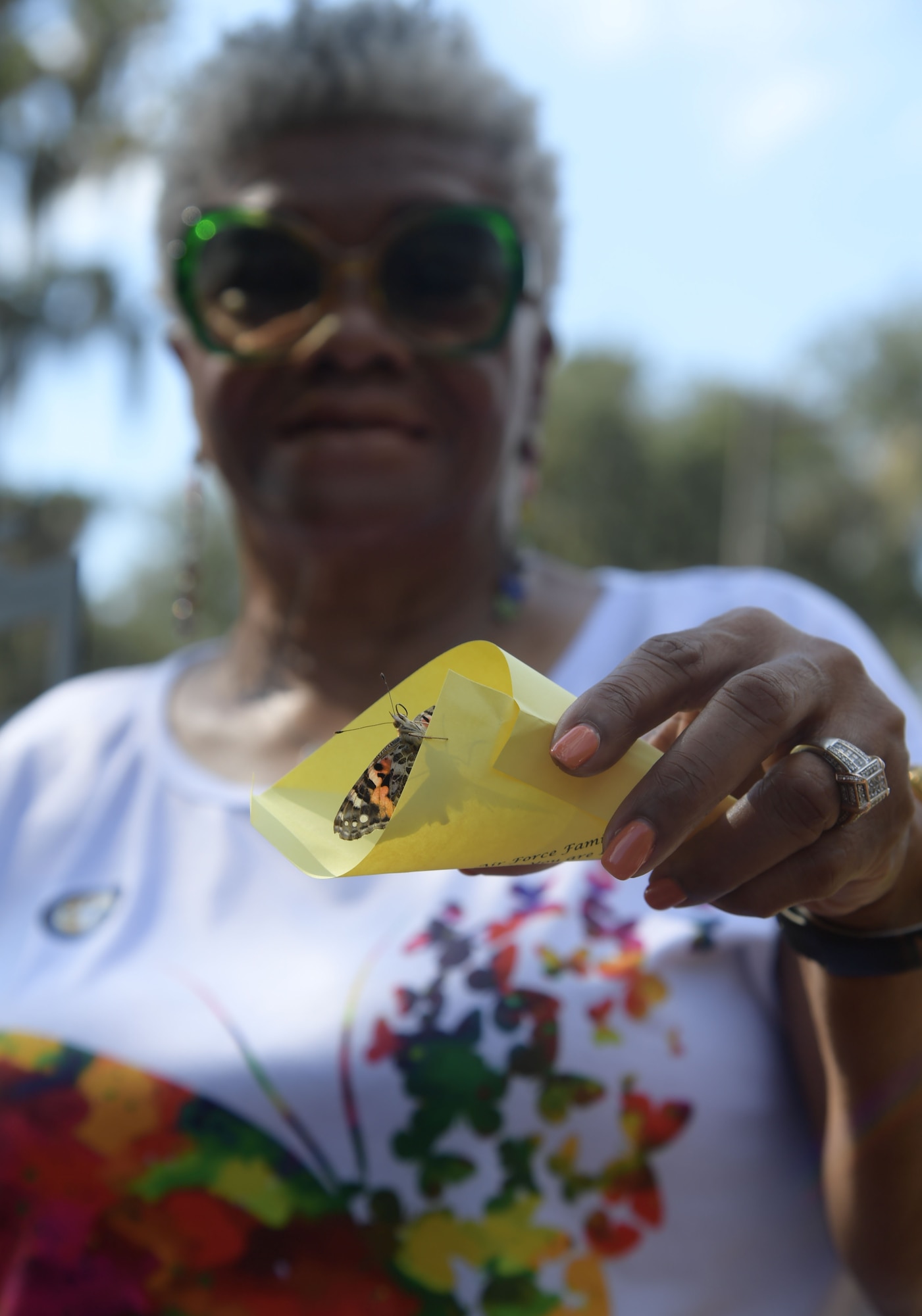A woman holds out a butterfly about to be released from a yellow piece of paper.